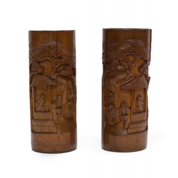 Deux vases bruns en bois sculpté. Des images sont sculptées dans les vases. Elles représentent trois hommes barbus se tenant près d’une structure couverte, avec un arbre en arrière-plan. Les images en relief sur les vases sont des images miroirs l’une de l’autre.