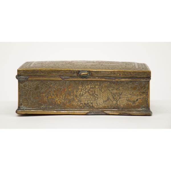 A brass trinket box with a clasp on the front side. There are four figures etched into the box. The box is tarnished along the edges.