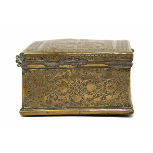 The side of a brass trinket box with a symmetrical floral decoration. The edges of the box are tarnished. 