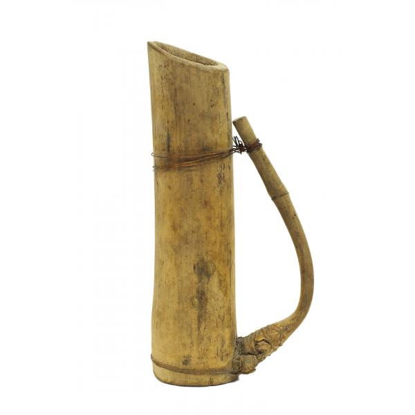 A light brown pitcher made from bamboo, with a handle facing right. The handle is made from a branch growing off of the trunk that was bent back and secured with copper wire.