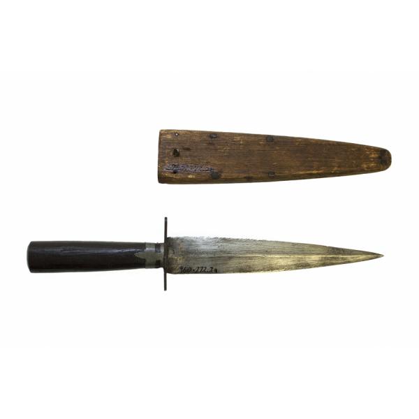 Dague en métal avec une lame symétrique et un fourreau en bois, pointant vers la droite. La dague est munie d'un manche en bois foncé et de deux rangées de points le long de la lame. Le fourreau en bois brun comporte quatre clous de chaque côté le long du bord. 