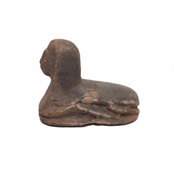 The side of a brown ceramic, human-headed scarab facing left. Its folded wings are visible, as is the profile of the head and headdress.  
