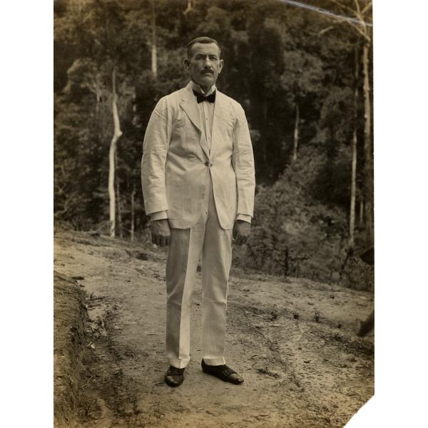 Une photo de William O. Gillespie portant un costume blanc avec un nœud papillon foncé. Il se tient sur un sentier devant les arbres. 