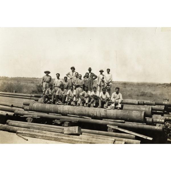 A photo of a group of men standing and sitting on a pile of casing. There is a mixture of International Drillers and labourers. 