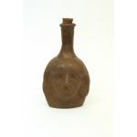 Front side of a clay anthropomorphic jug showing the face. The spout has a clay stopper in it.
