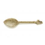 The front of an ivory-carved spoon with a point on the end. It is speckled with brown dots and the top of the handle is shaped like a bud. 