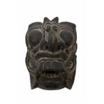 The front of a demon mask. It has large eyes, ears, a nose, and a mouth with large teeth. 