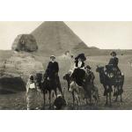 A postcard of four people riding three camels and a donkey in front of the Sphinx and a pyramid. 