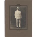 William McRae standing in a white suit and panama hat. Photograph is placed in a brown matte. 