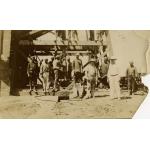 A photo of a group of men standing in front of the base of a wooden derrick. There are two International Drillers standing in the front, wearing white outfits and pith helmets.