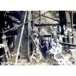 Two International Drillers standing behind six seated labourers inside of an oil rig. There are metal and wood beams around them.