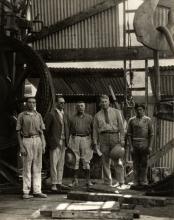 Group of five oil drillers in their dirty clothes standing inside a rig. George Rawlings is the second from the right.