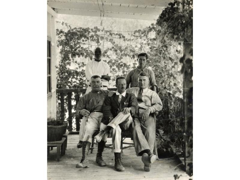 Group of five men, three sitting, on a shaded veranda. George Rawlings is sitting on the right.