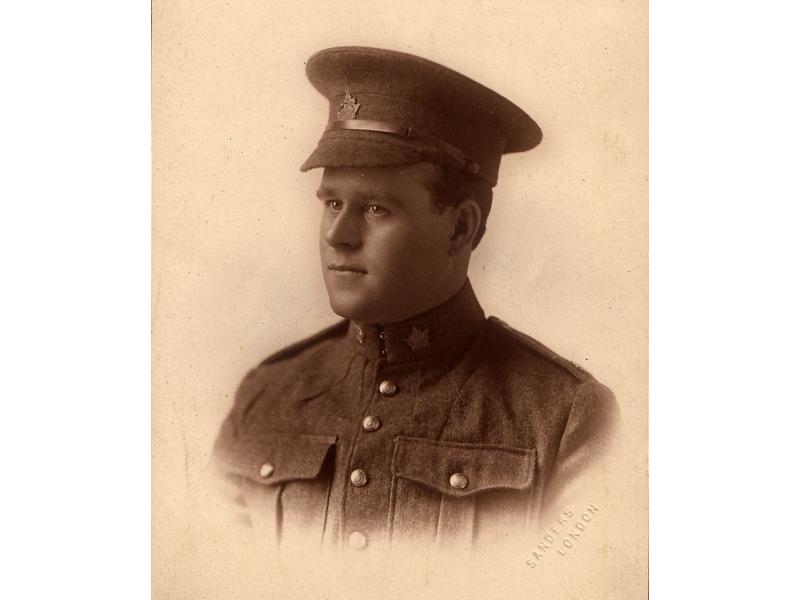 Harry Brown wearing a military uniform with maple leaf insignia on the collar of his jacket and on his hat. He is clean-shaven and has a round face.