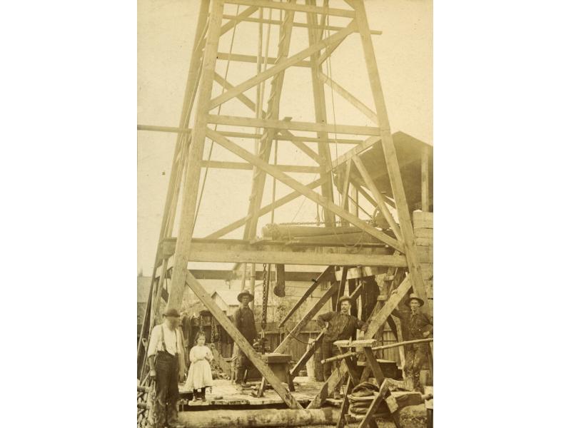 A Canadian Pole-Tool Drilling Rig, which is  wooden oil rig with  four legs and crossbeams moving up its height.