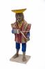 Vue avant de la figurine d’une femme portant une cruche d’eau sur son dos. Elle porte des sandales, un costume bleu et un poncho de différentes couleurs, ainsi qu'un couvre-chef rose et un chapeau retourné jaune et orange.