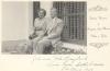 Vola and John Braybrook sitting on a windowsill. There are bars on the window and flowers by their feet. The photo is part of a Christmas card. 
