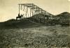 A photo of a man on a horse looking at a steel derrick lying on its side in the dirt.