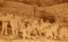 A photo of two rows of International Drillers, all wearing white, sitting in front of a long log that is taller than the men.