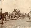 Une photo de charrettes tirées par des chevaux et remplies de marchandises. Des hommes qui montent sur l'une des charrettes et d'autres hommes sont à cheval.