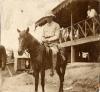Une photo d’un foreur international vêtu de blanc, coiffé d’un casque colonial et assis sur un cheval. Il est devant un bâtiment monté sur pilotis.  