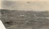 Une photo d’une route sillonnant le désert, avec des collines en arrière-plan. Il y a un bâtiment au centre de la photo. 