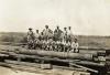 A photo of a group of men standing and sitting on a pile of casing. There is a mixture of International Drillers and labourers. 